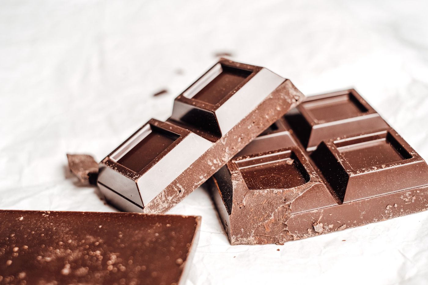 Carrés de chocolat noir cassés posés sur un papier blanc froissé