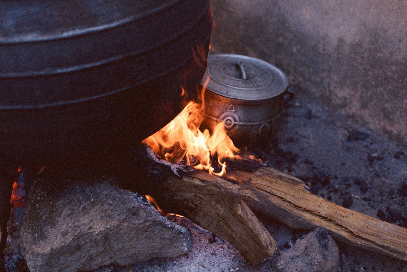 Marmites en fonte chauffées par un feu de bois posé entre des pierres, en plein air